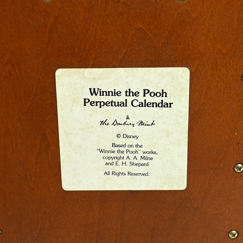 335 - A Danbury Mint Winnie The Pooh perpetual calendar, on a wooden display cabinet 