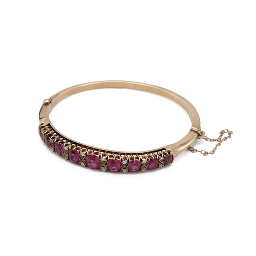 203 - An early 20th-century synthetic ruby and diamond hinged bangle, set with nine graduated oval cuts wi... 