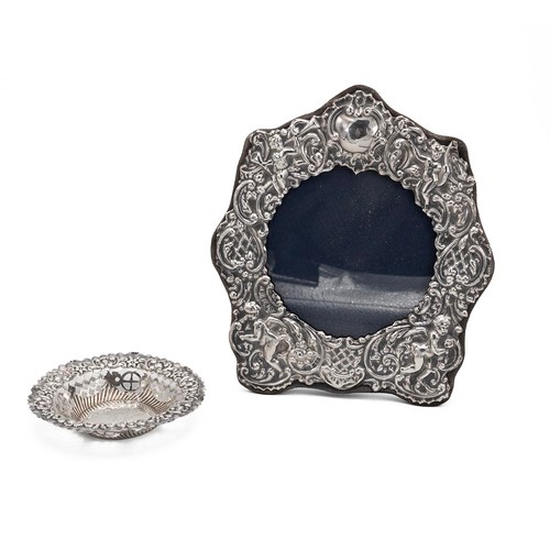 28 - Silver photograph frame and a silver pin dish. The frame decorated with cherubs and foliate decorati... 