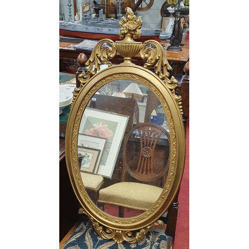 33 - A 20th Century Gold coloured mirror of oval form with cartouche top and base.