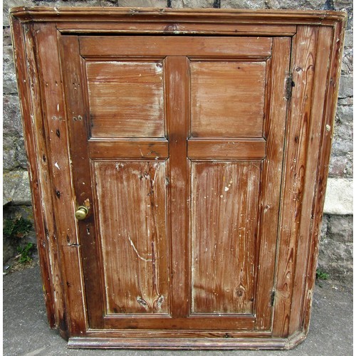 1054 - A 19th century stripped pine hanging corner cupboard enclosed by a single moulded panelled door with... 