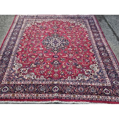 858 - A large Red ground hand woven Persian Mashhad Carpet with a central medallion design and a surroundi... 