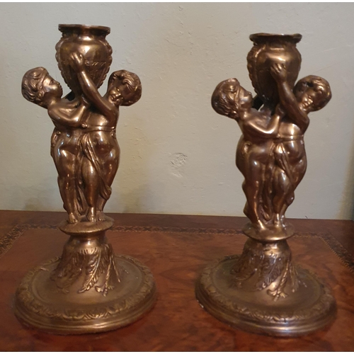 53 - A pair of 20th Century Brass Candlesticks depicting two cherubs holding up an urn. H 25 cm approx.
