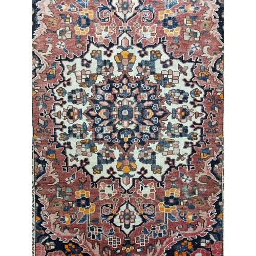 1083 - A good Terracotta ground hand woven Persian Carpet with a traditional medallion design from the Bakh... 