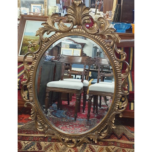 84 - A reproduction timber gilt oval Mirror with a highly carved outline and cartouche top. 125 x 93 cm a... 