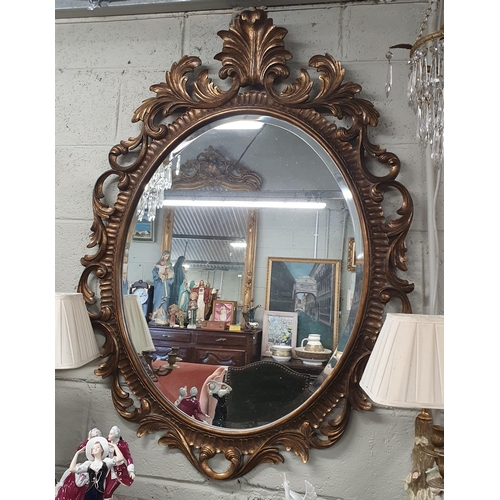 84 - A reproduction timber gilt oval Mirror with a highly carved outline and cartouche top. 125 x 93 cm a... 