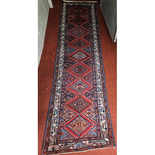 61 - A Red ground full pile handwoven Persian Mishkin Runner with a diamond medallion design. 313 x 90 cm... 