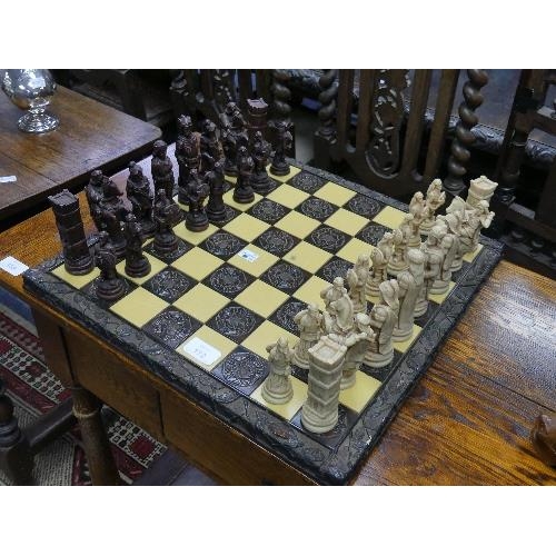 172 - A resin Chess Set, the board with carved wooden frame, 17¾in (45cm) wide.