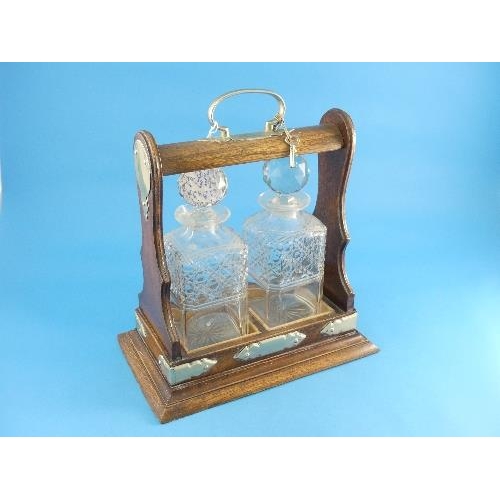 174 - An Edwardian oak two-bottle Tantalus, with silver-plated mounts, both cut-glass bottles chipped, 13i... 