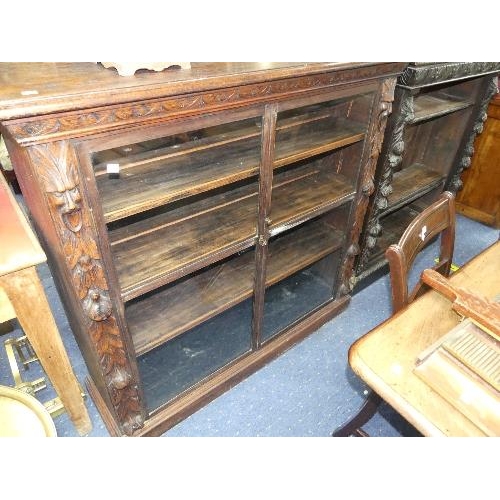 100 - An early 20thC carved oak glazed Bookcase, with two glazed doors and lion head, mask and fruiting de... 