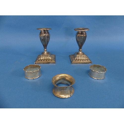 63 - Three silver Napkin Rings, all a/f, 1ozt, together with a pair of silver plated short candlesticks, ... 