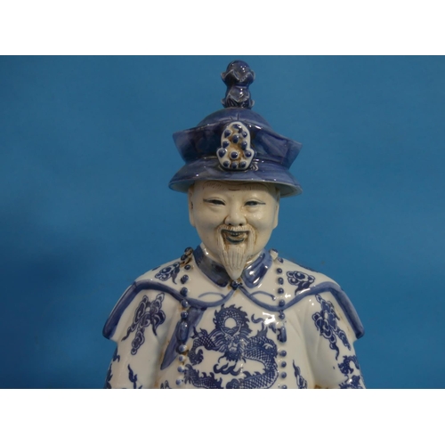 111 - A 20th century Chinese blue and white porcelain figure of an Elder, behatted and holding a pipe, his... 