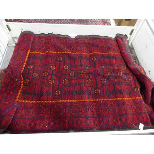 394 - Tribal rugs; an old Turkmen Kurdish red ground rug, coarsely woven and hand-knotted with four centra... 