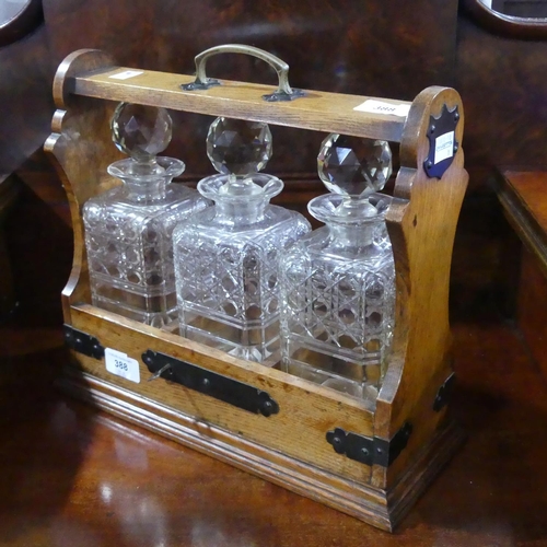 388 - An early 20thC oak Tantalus, comprising three glass decanters, all chipped, locking mechanism, with ... 