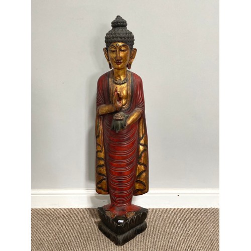 531 - A Thai carved and gilt wood standing figure of a priest, holding a flower in one hand, on triangular... 