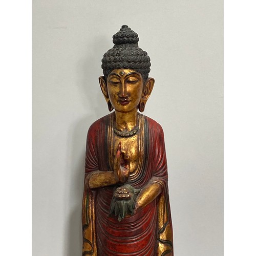 531 - A Thai carved and gilt wood standing figure of a priest, holding a flower in one hand, on triangular... 