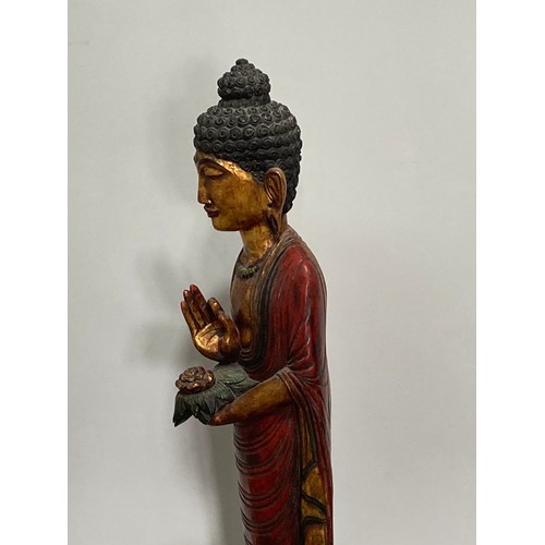 531 - A Thai carved and gilt wood standing figure of a priest, holding a flower in one hand, on triangular... 