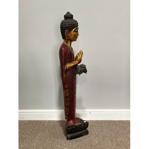 531 - A Thai carved and gilt wood standing figure of a priest, holding a flower in one hand, on triangular... 