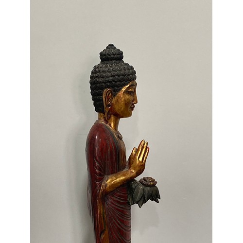 531 - A Thai carved and gilt wood standing figure of a priest, holding a flower in one hand, on triangular... 