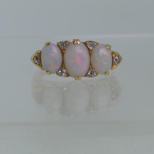 An early 20thC graduated three stone opal Ring, each with two diamond points set vertically  between and with a further diamond point on each shoulder, the centre opal 8mm x 6mm, all mounted in 18ct yellow gold in a scroll gallery, Size L, approx total weight 6.3g.