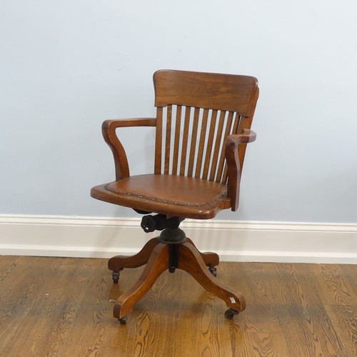 391 - An early 20thC oak open arm swivel Desk Chair, with leather upholstery and paper label, raised on sp... 