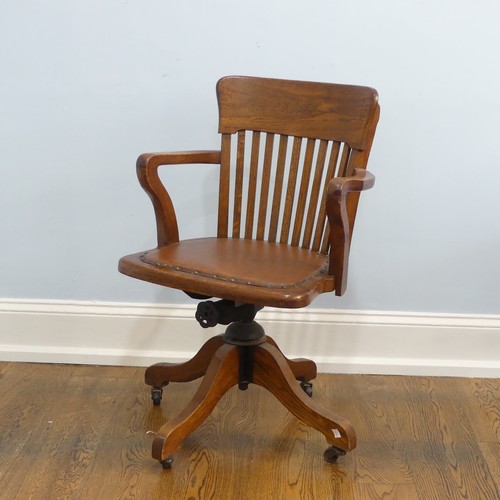 391 - An early 20thC oak open arm swivel Desk Chair, with leather upholstery and paper label, raised on sp... 