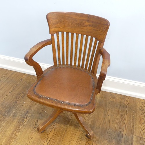 391 - An early 20thC oak open arm swivel Desk Chair, with leather upholstery and paper label, raised on sp... 