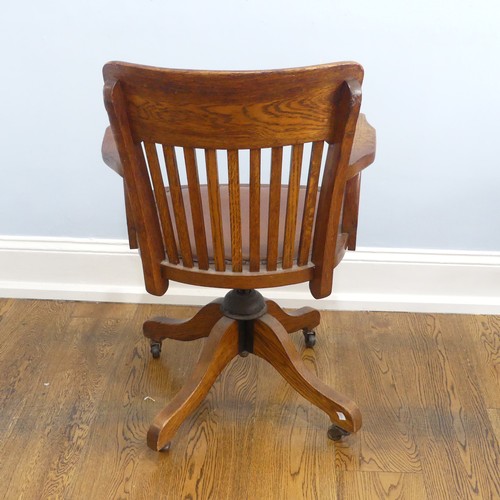 391 - An early 20thC oak open arm swivel Desk Chair, with leather upholstery and paper label, raised on sp... 