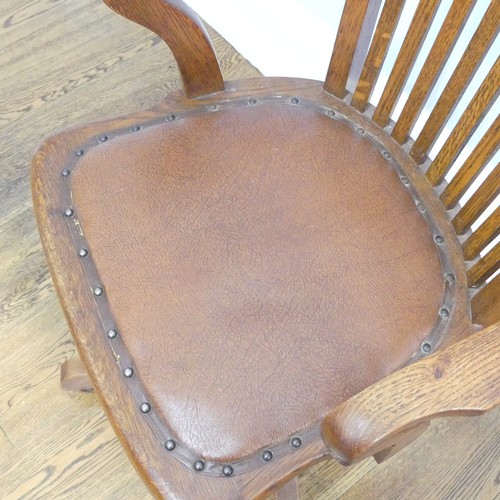 391 - An early 20thC oak open arm swivel Desk Chair, with leather upholstery and paper label, raised on sp... 