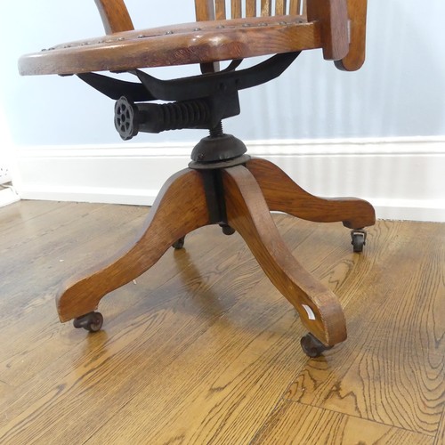 391 - An early 20thC oak open arm swivel Desk Chair, with leather upholstery and paper label, raised on sp... 