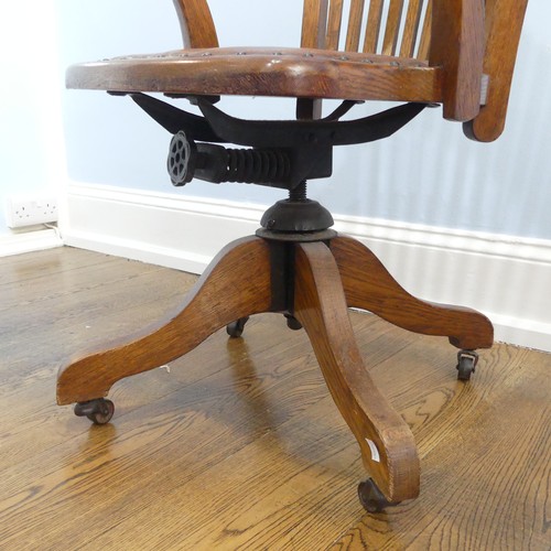 391 - An early 20thC oak open arm swivel Desk Chair, with leather upholstery and paper label, raised on sp... 