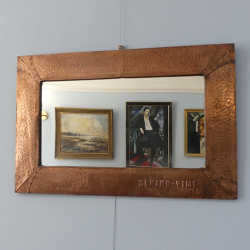 An Arts and Crafts copper framed rectangular Wall Mirror, hammered and riveted surround with motto 'Behind Time' to lower right, partial paper label to verso, W 82cm x H 53cm.