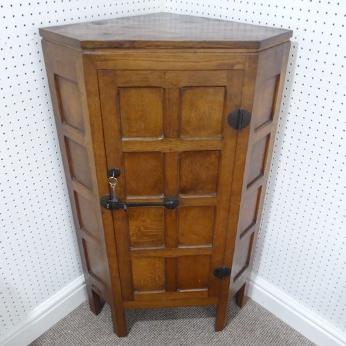 Robert Mouseman Thompson (1876-1955), an oak panelled floor standing Corner Cupboard, 1930's,  the door with wrought iron hinges and latch with square-head screws, the interior with three shelves, top shelf shaped, on five stile feet, recessed carved mouse trademark, 68cm wide x 47cm deep x 115cm high.