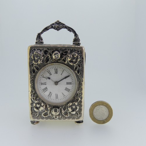 A late Victorian silver miniature carriage Timepiece, by Mappin & Webb, hallmarked London, 1895, with white enamel dial and Roman Numerals, the case with foliate decoration and raised on bun feet, the hinged rear cover revealing the unsigned movement with platform escapement, currently running, 10cm high to top of carry handle.