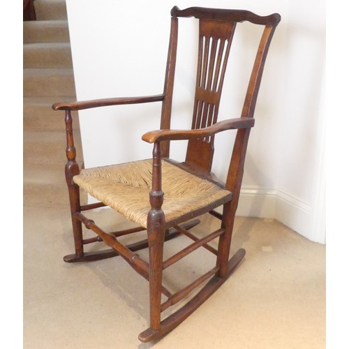 654 - A George III Rocking Chair, having a pierced back above a rush seat, raised on turned legs joined by... 