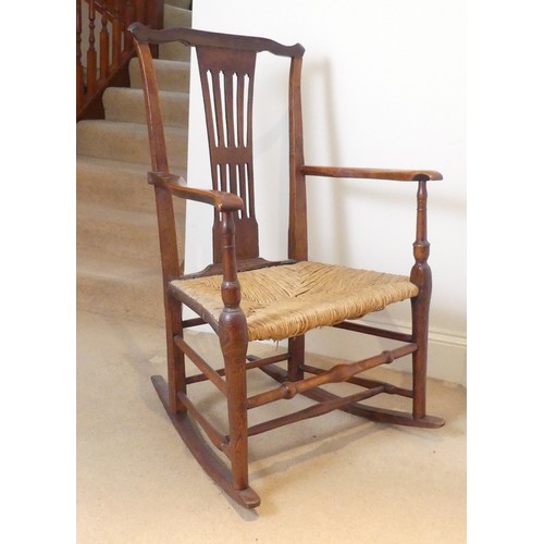 654 - A George III Rocking Chair, having a pierced back above a rush seat, raised on turned legs joined by... 