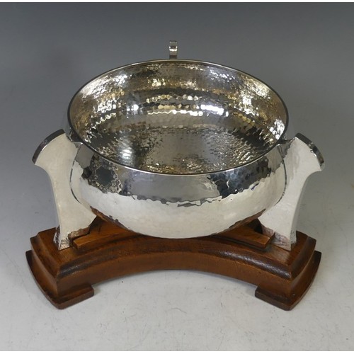 A George V silver 'Tyg' Bowl, by Barker Brothers, hallmarked Chester 1912, of circular form with three stylised handles continuing to form raised supports, the whole with hammered decoration, 18cm bowl diameter, 11cm high, 18.3ozt, raised on oak base in the Arts & Crafts style.