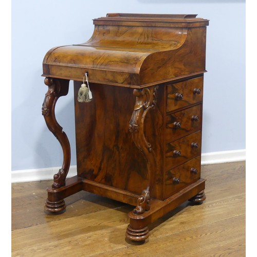 A Victorian walnut pop-up piano-top Davenport desk, the hinged rectangular top with three-quarter gallery raising to reveal three small drawers and pigeonholes, above a further hinged cover enclosing a sliding plateau with inset writing surface, angle-adjustable on a ratchet, small drawers and stationery compartments, the side with four drawers and opposing dummy drawers, carved scrolled supports, turned feet and recessed brass casters, 96cm raising and opening to 110cm high, 60cm wide, 58cm deep.