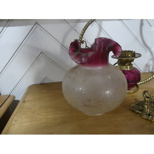 303 - A Victorian hanging brass Oil Lamp, having a cranberry glass font and shade, one brass ornament brok... 