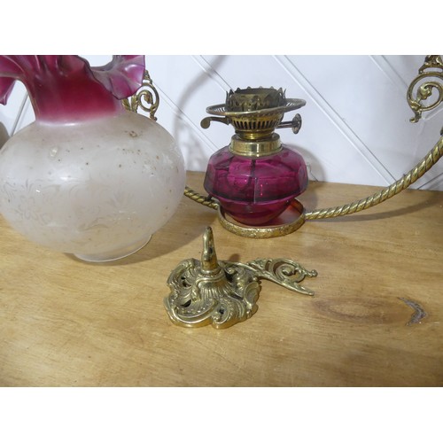 303 - A Victorian hanging brass Oil Lamp, having a cranberry glass font and shade, one brass ornament brok... 