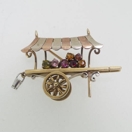 113 - A charming 9ct tri-colour gold Brooch, in the form of a hand cart, with rotating wheels, set with ha... 