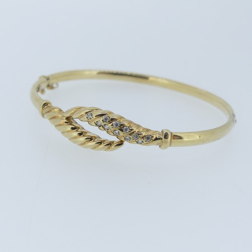 388 - A 9ct gold hollow hinged Bangle, the cross over front set white pastes, approx total weight 7.6g.... 