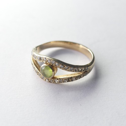 325 - A peridot and diamond Ring, the split front with central collet set peridot with a row of diamond po... 