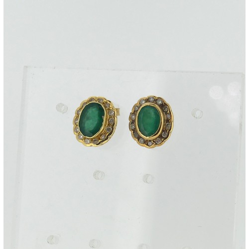 447 - A pair of emerald and diamond cluster Earrings, the central oval emerald approx. 7mm long, collet se... 