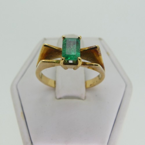 107 - A small emerald Ring, the emerald cut stone 5.9mm long, four claw set in a modernist 18ct gold shank... 