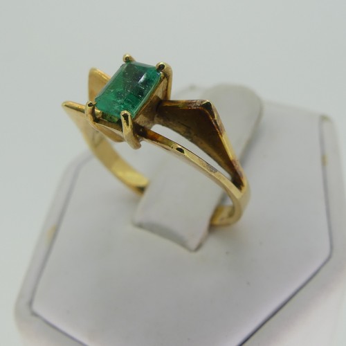 107 - A small emerald Ring, the emerald cut stone 5.9mm long, four claw set in a modernist 18ct gold shank... 