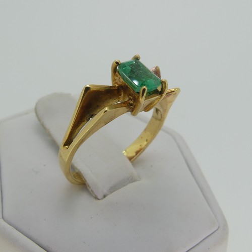 107 - A small emerald Ring, the emerald cut stone 5.9mm long, four claw set in a modernist 18ct gold shank... 