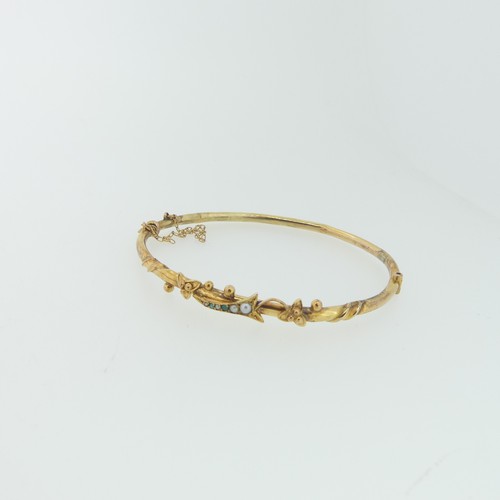 250 - A narrow 9ct gold hollow hinged Bangle, the front with stylised foliate decoration set seed pearls a... 