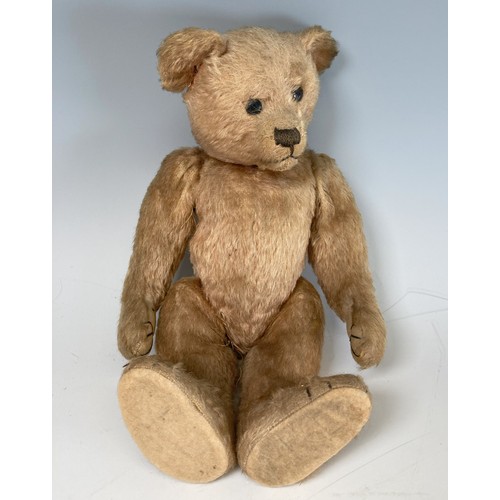 A vintage Teddy Bear, with black button eyes, straw filling, sewn nose, light orange plush and felt pads, 14in high.