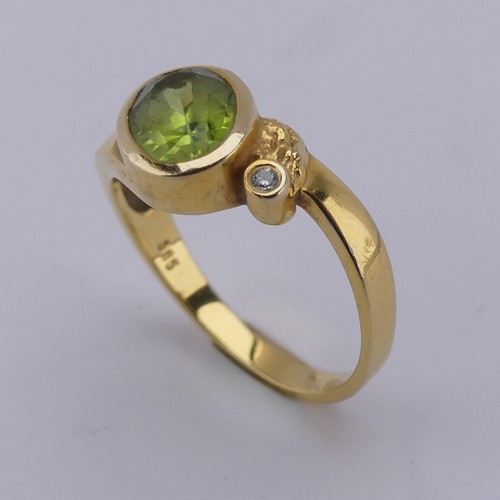 169 - An oval facetted peridot Ring, collet set in 14ct yellow gold with diamond point accent, Size M, 3.3... 